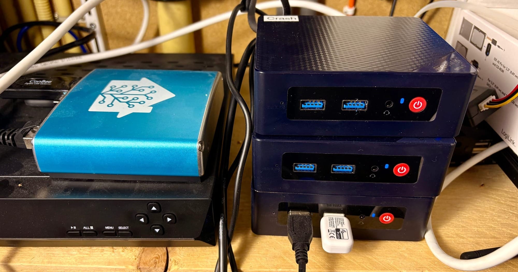 A Home Assistant Blue device next to a stack of three mini PCs labeled “Crash,” all wired in a network setup.